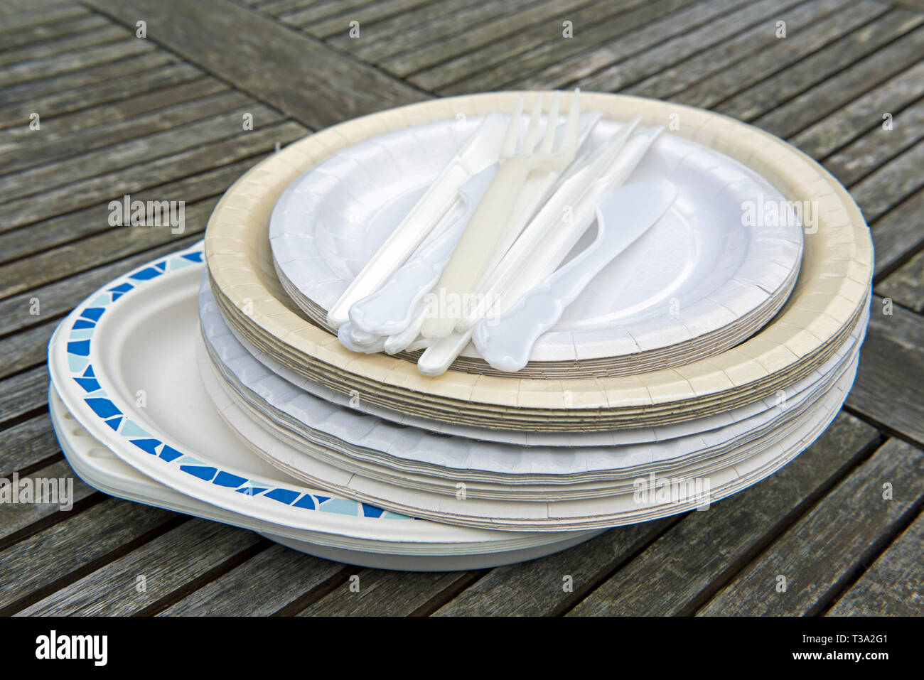 Assorted paper plates with plastic cutlery on garden table. Stock Photo