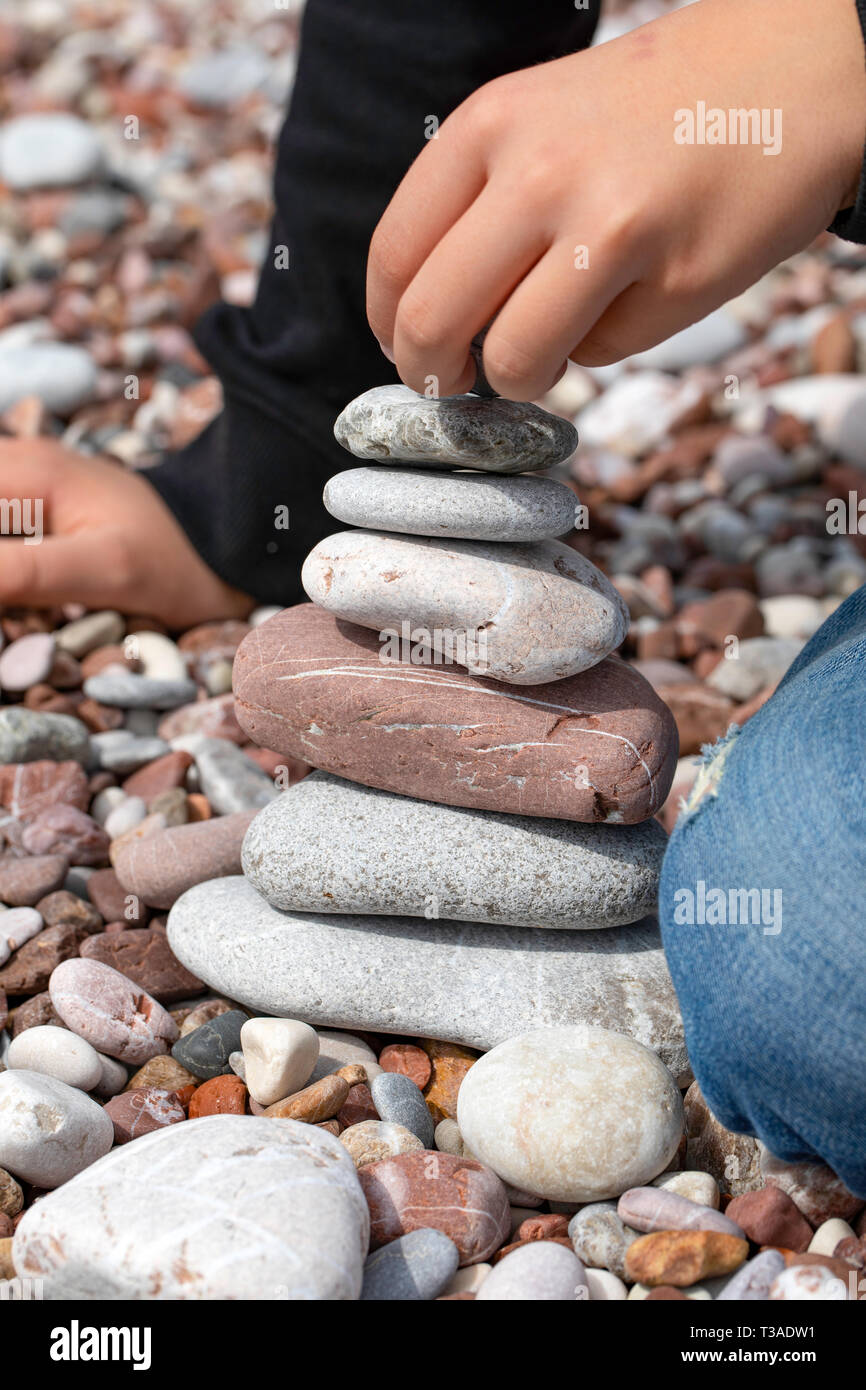 Boy building a stone pyramid, beach in Sveti Stefan, Montenegro. Stone balancing. Stock Photo