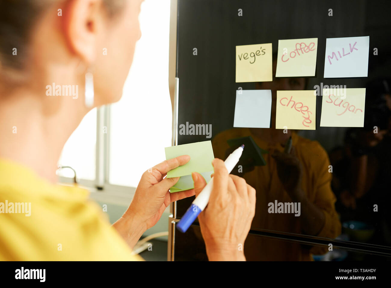 Woman sticking notes with products on refrigerator Stock Photo