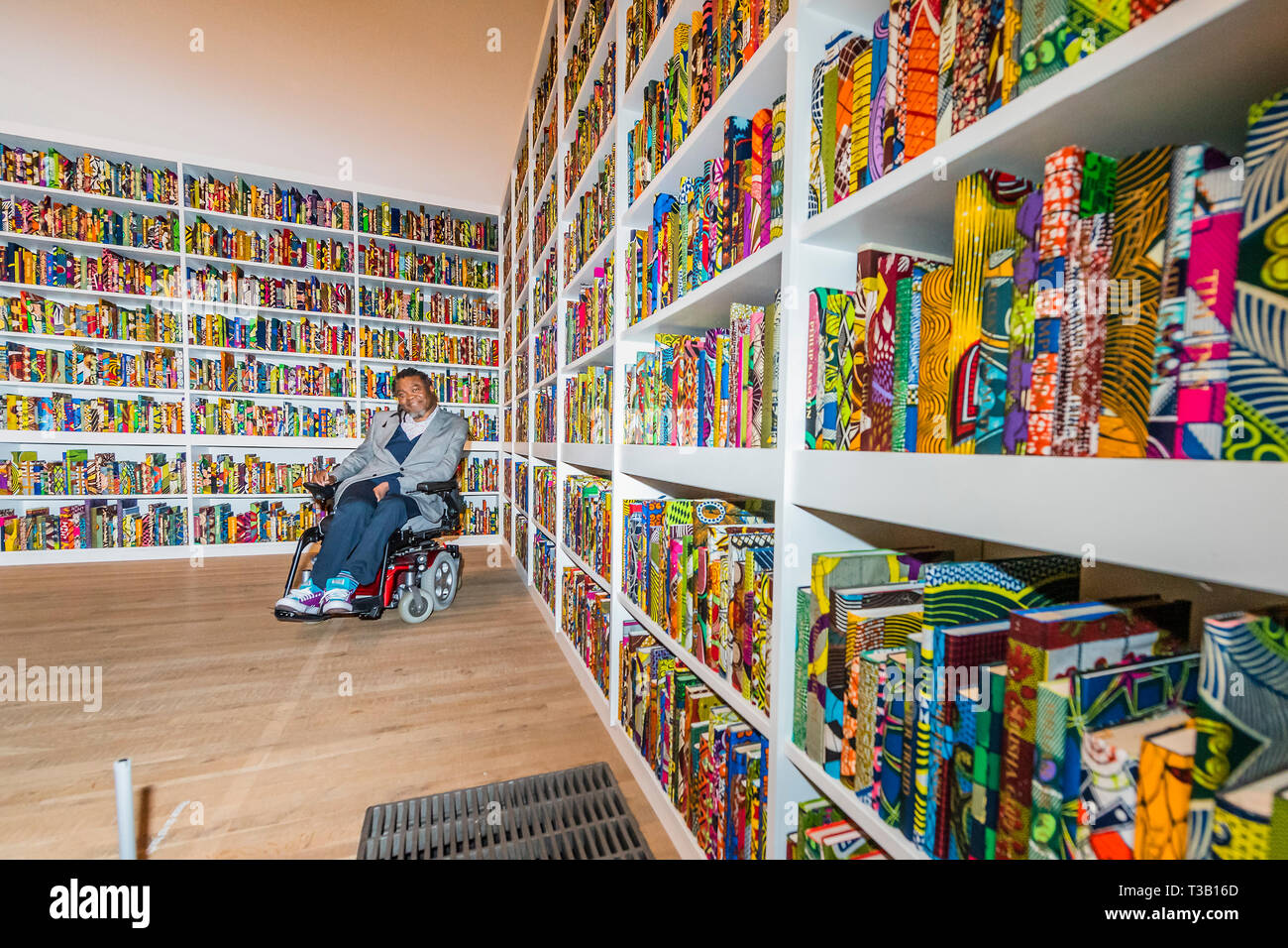 London, UK. 08th Apr, 2019. The British Library an installation by Yinka Shonibare CBE (pictured with his work), at Tate Modern, having just been acquired by them. Highlighting the impact of immigration on British culture, it is a site-specific installation with a digital platform for visitors to join in the discussion.It contains 6,328 books bound in ‘Dutch wax print. The installation also contains an area for audiences to access information about the project on tablets. Credit: Guy Bell/Alamy Live News Stock Photo
