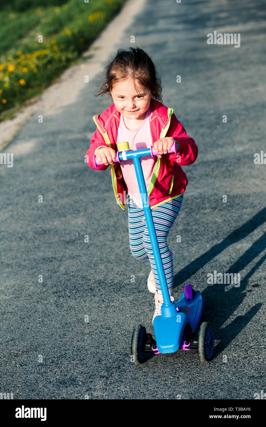 Little adorable girl having fun riding on scooter, playing outdoors Stock Photo