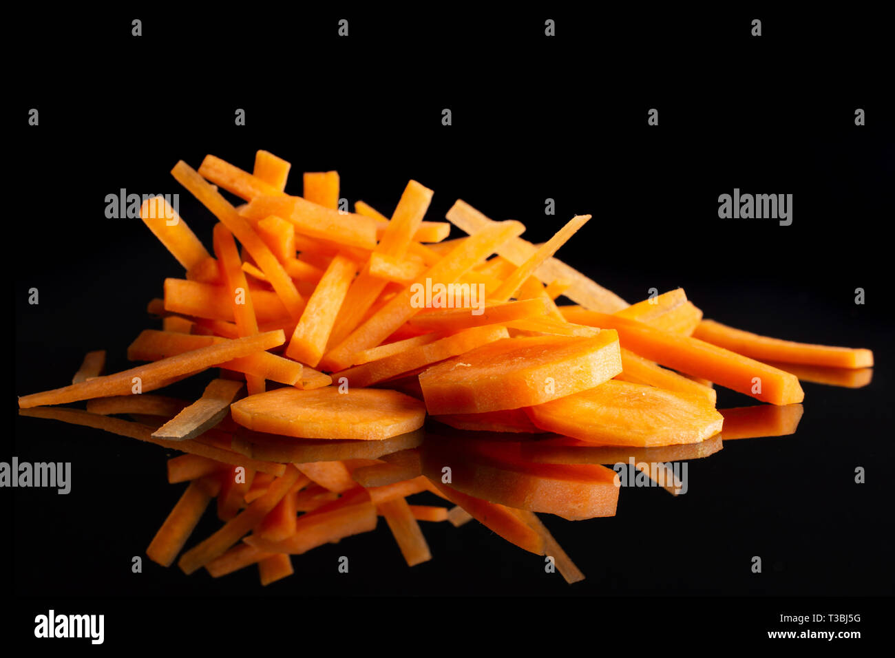 Group of five slices lot of pieces of fresh orange carrot thin noodles and round slices isolated on black glass Stock Photo