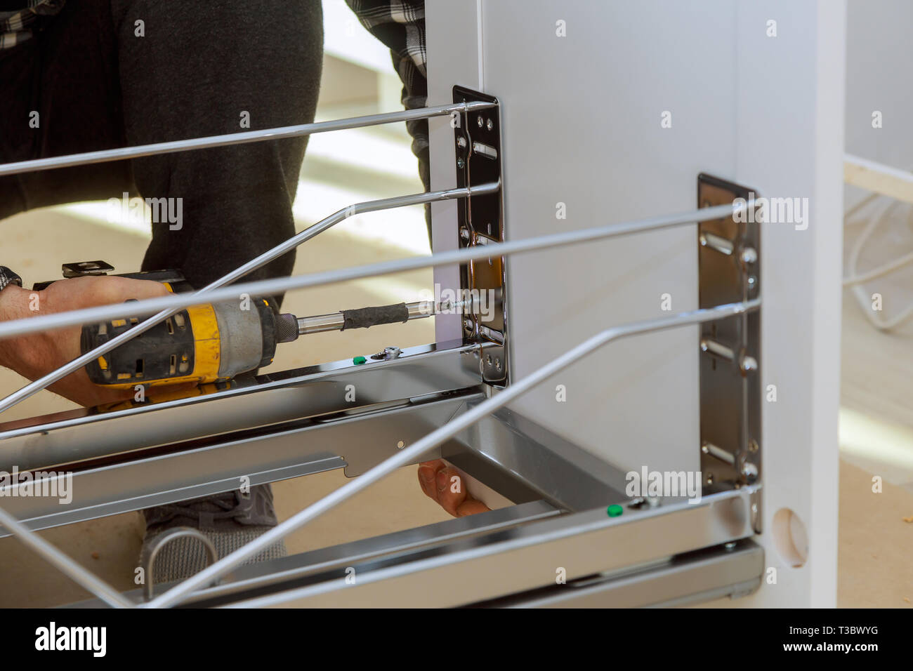 Assembling furniture woodworker screwing using a cordless screwdriver drawers garbage bin in the kitchen Stock Photo