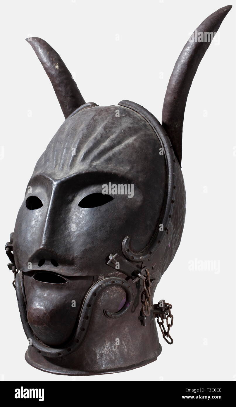 A mask of shame, Historism period in the style of the 16th century Large, elaborately hammered, iron mask in the shape of a devil's head. One-pieced hammered bowl with riveted devil horns and neck. Hinged, pivoted visor with stylised facial features and continuous, riveted hollow beads, securable by hasps and cotter pins. Pivoted chin with mouth opening, decorated also with a riveted hollow bead and secured with two hasps (one is missing). Height with horns 49 cm. Work with a lot of passion for detail, very decorative object. historic, historical, Additional-Rights-Clearance-Info-Not-Available Stock Photo