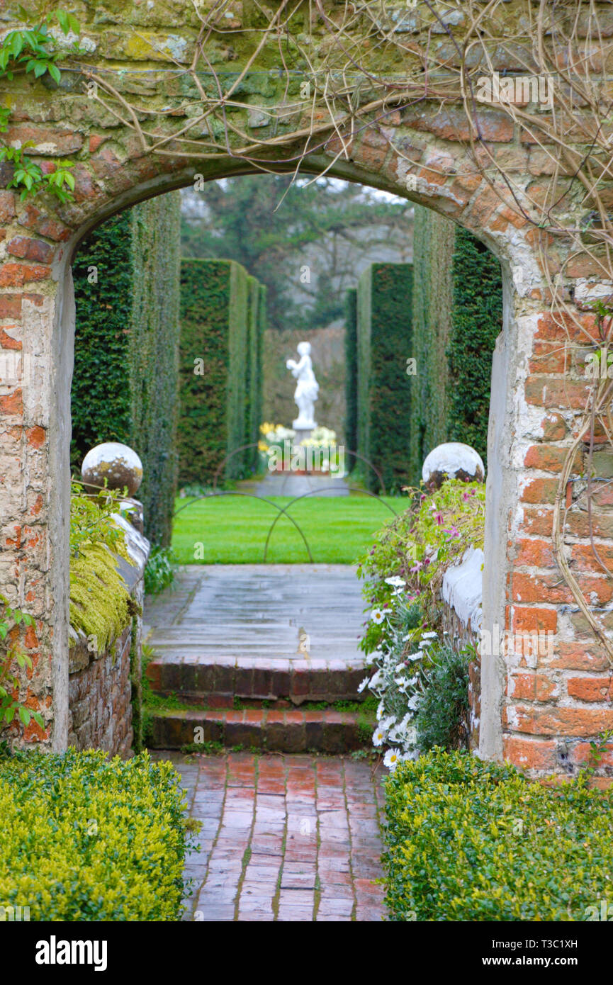 View through an English garden gate to a marmoreal sculpture between shrubs of box trees. Stock Photo