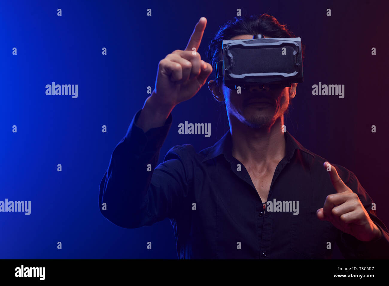 Young serious man in shirt using a virtual reality headset standing and gesturing over black background Stock Photo
