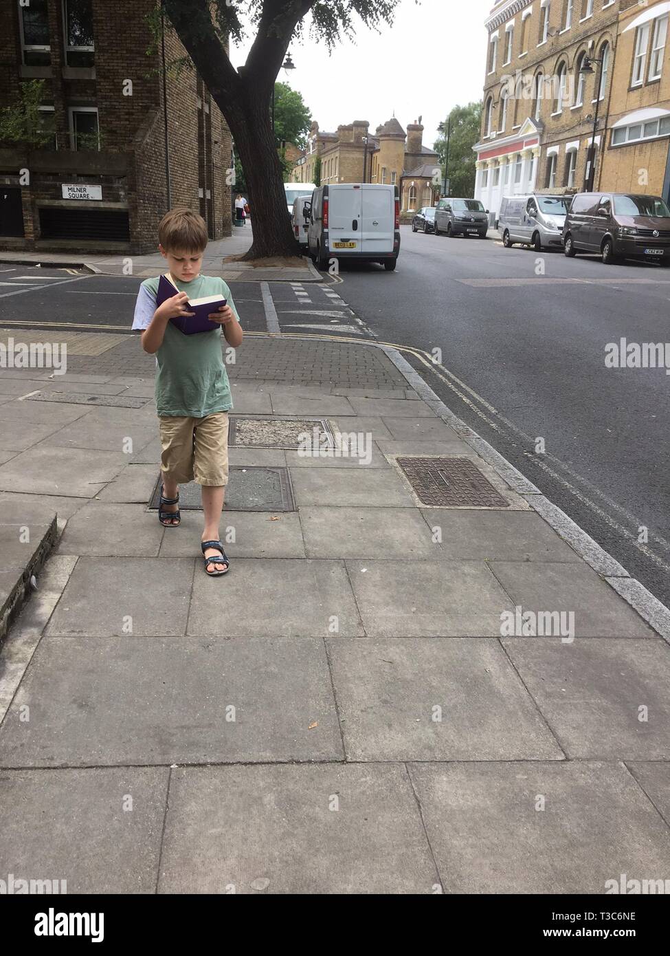 9 year old walking along the pavement while reading a book Stock Photo
