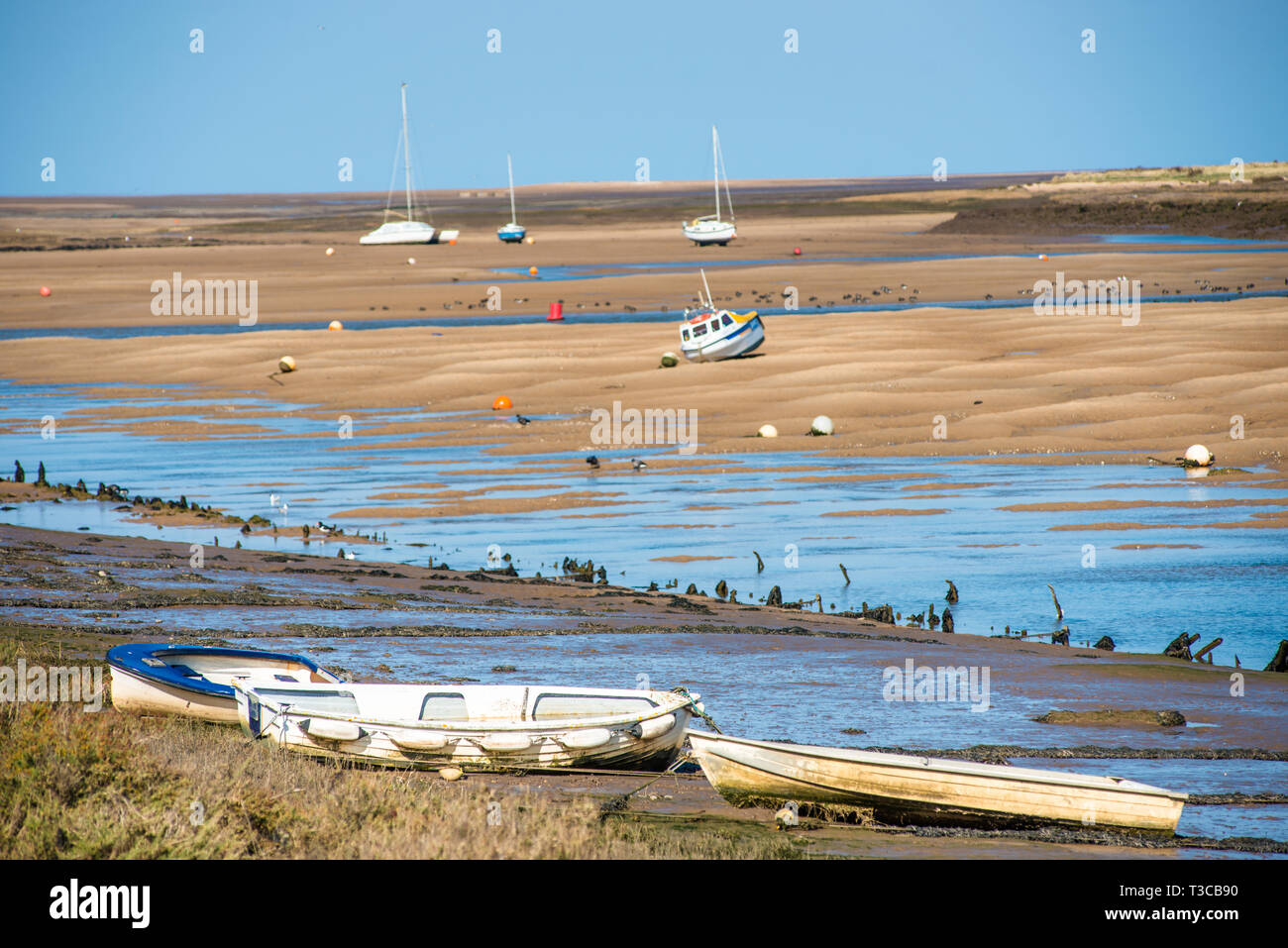 Colourful boats marooned on sandbanks at low tide on East Fleet river estuary at Wells next the sea, North Norfolk coast, East Anglia, England, UK. Stock Photo