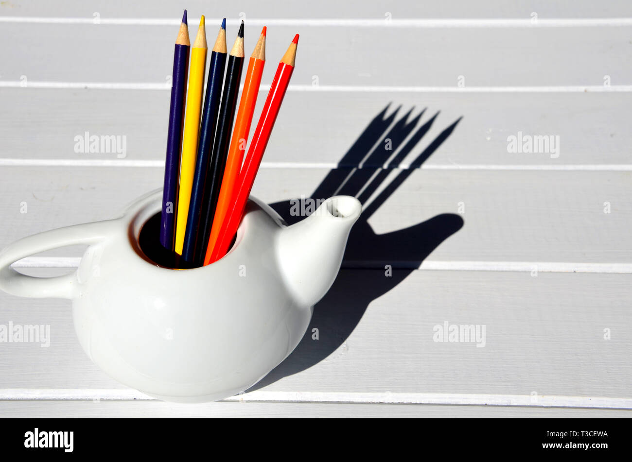 Set of wooden colored pencils in a white bowl, on a wooden table Stock Photo