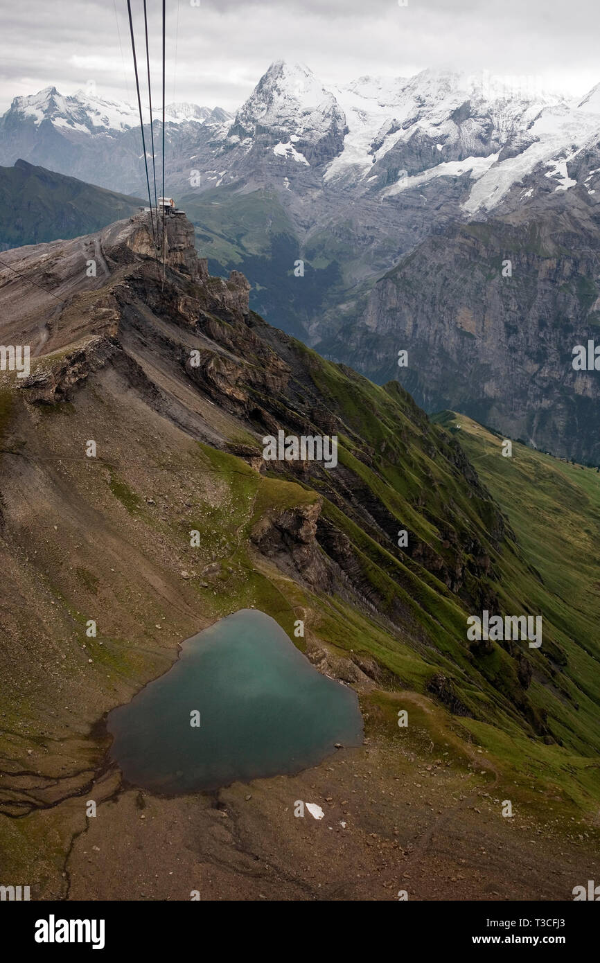 The Birg cablecar station perched above a cliff with the Jungfrau Massif and the Lauterbrunnen valley beyond and the Grauseeli, a small mountain tarn, Stock Photo