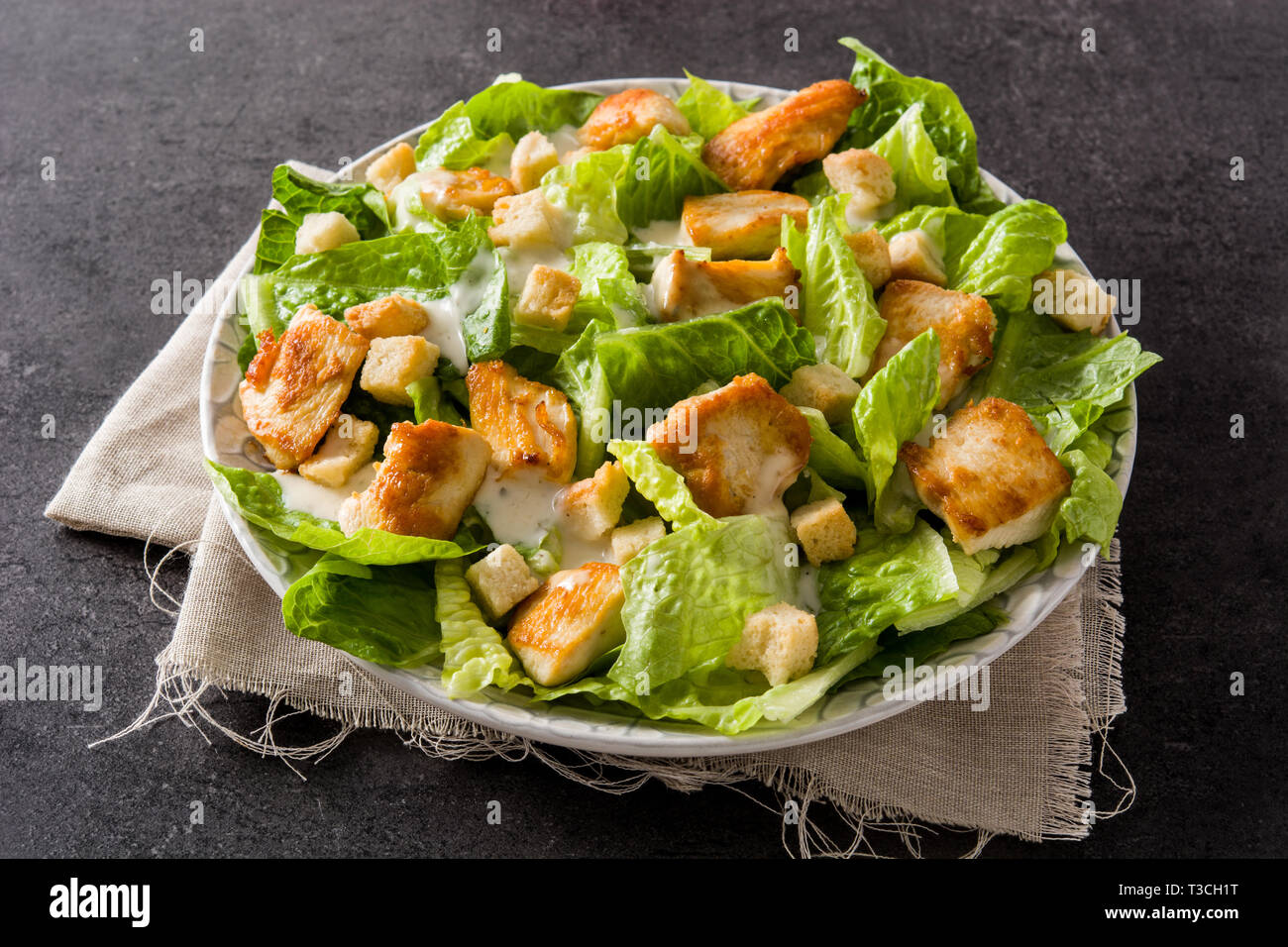 Caesar salad with lettuce,chicken and croutons on black background. Stock Photo