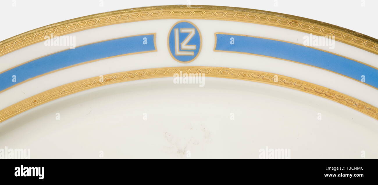 Four service pieces, from the on-board service of the LZ 127 'Graf Zeppelin', 1928 Heinrich & Co., Selb. Ivory coloured glazed porcelain with double blue and gold etched border décor and an vertically oval 'LZ' cartouche, On the bottom the underglaze green manufactory's mark with legend in red 'Heinrich-Elfenbein-Porzellan' and 'Graf Zeppelin 1928'. Consisting of a covered tureen with handles (height 14.5, diameter 22.5 cm), sauce boat (ca. 23.5 x 15.5 x 9 cm), oval service plate (32.5 x 23.5 cm), and a small bowl (height 4 cm, diameter 16.5 cm)., Additional-Rights-Clearance-Info-Not-Available Stock Photo