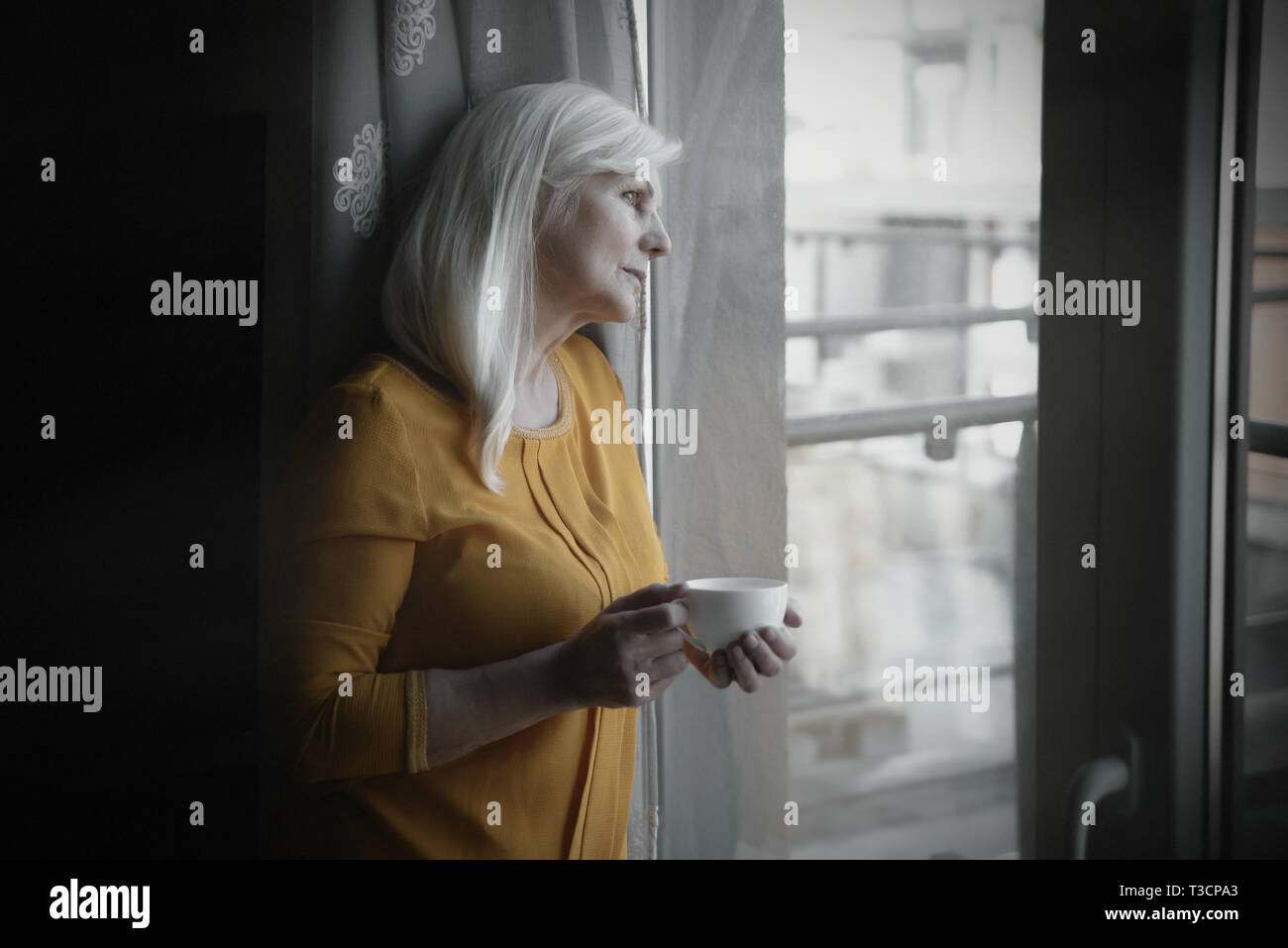 Depressed senior woman near window at home Stock Photo