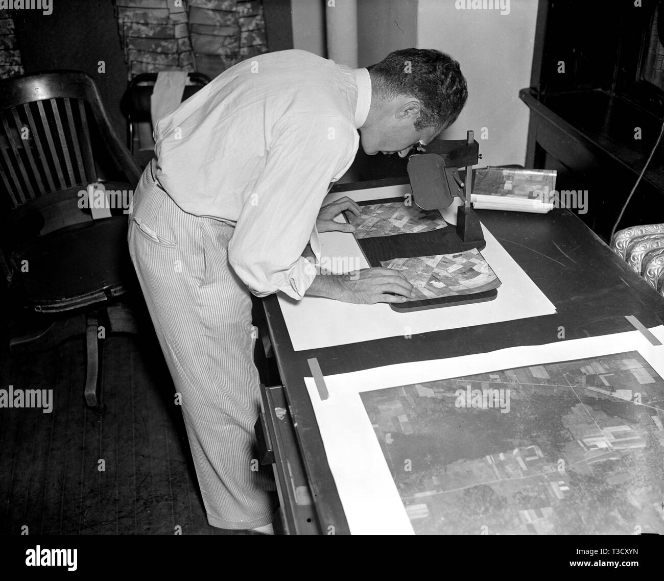 A worker is shown making a stereoscopic examination of the finished photographic prints to determine the relief or elevation of land surface for a map of the United States ca. 1937 Stock Photo