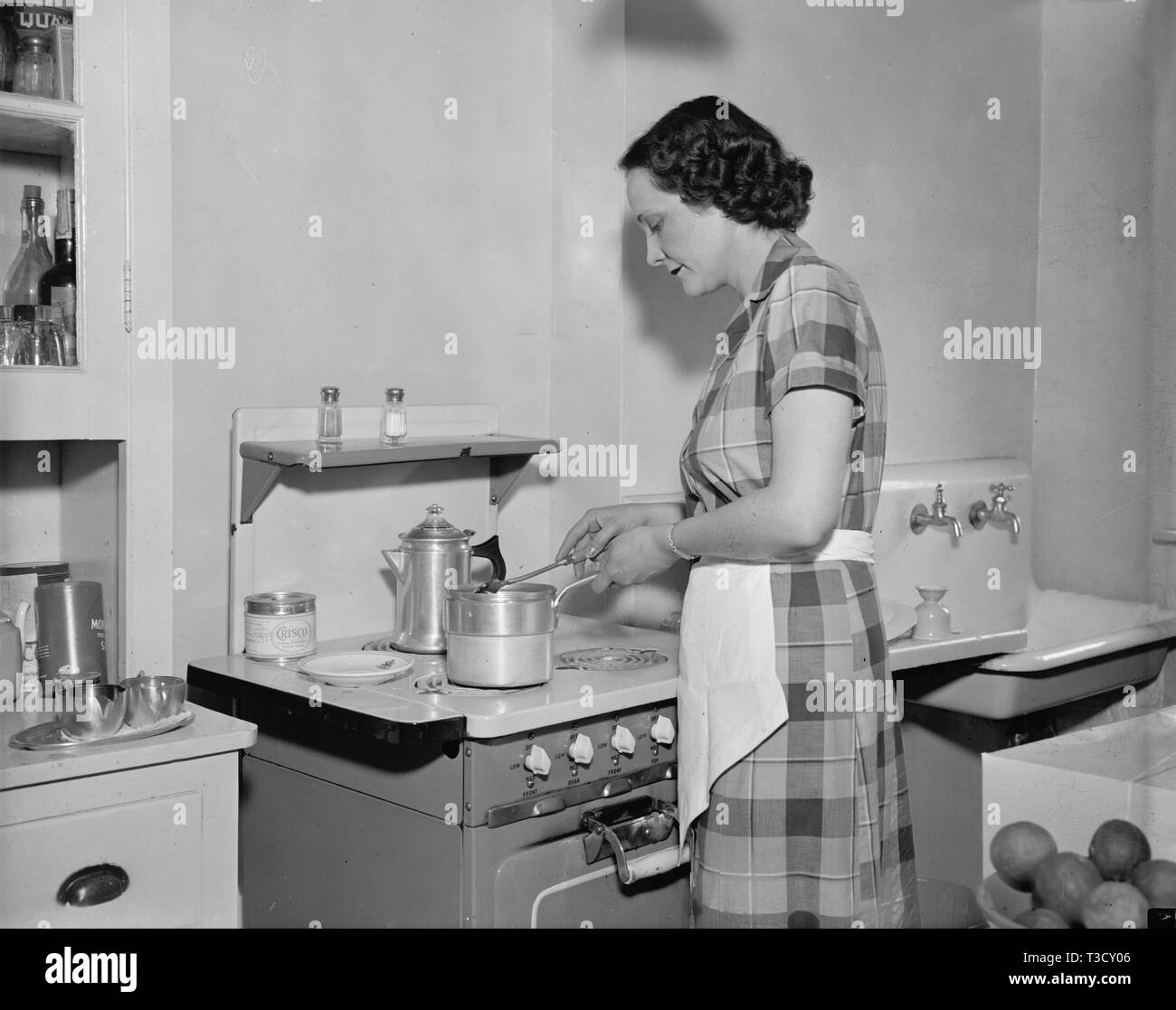 A woman cooking on a stove in the kitchen in 1937 Stock Photo