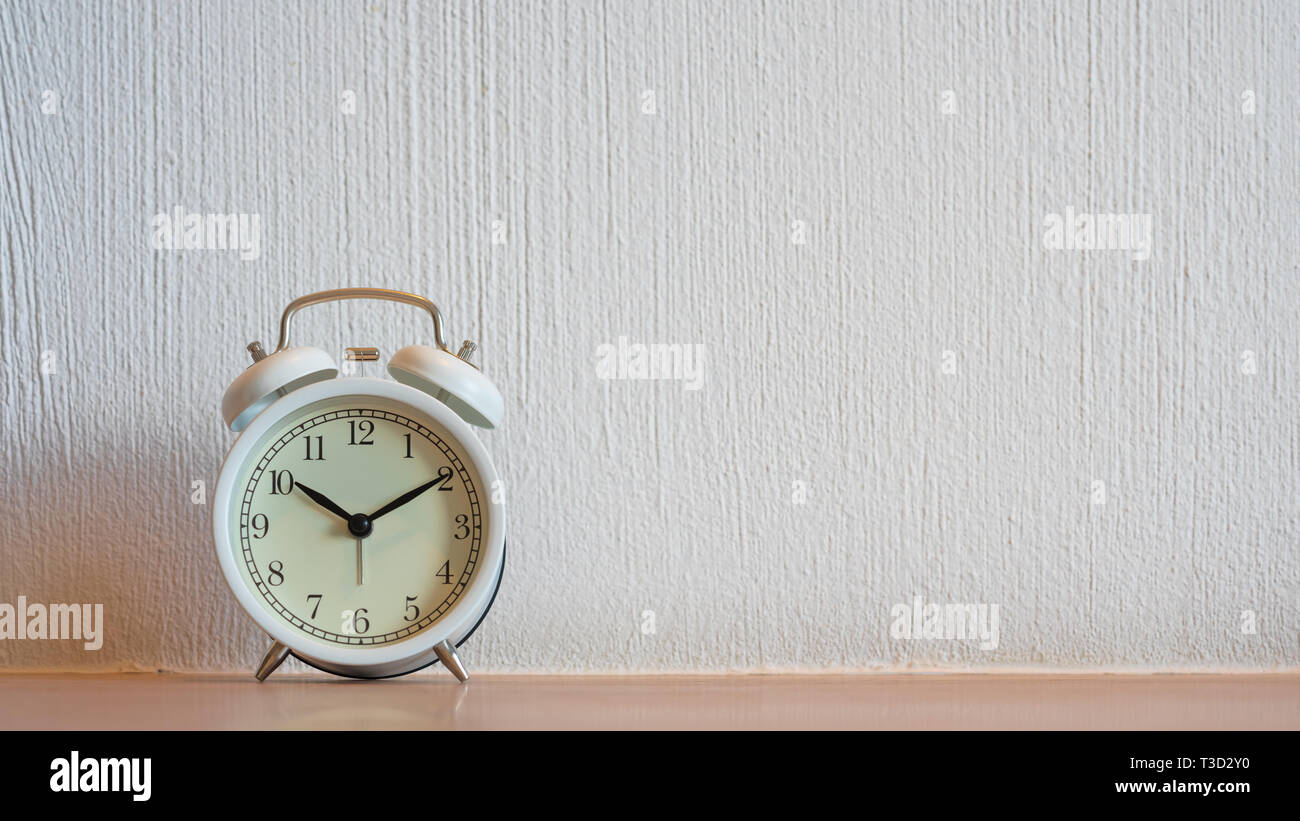 White vintage alarm clock displaying 1010 am or pm on wooden table and