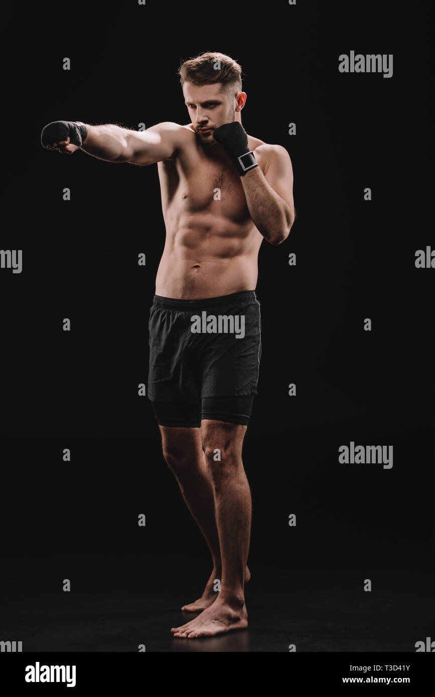 strong barefoot muscular mma fighter in bandages and shorts doing punch