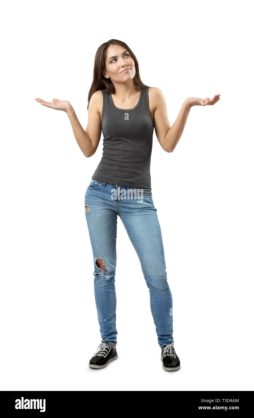 Young woman in gray top and blue jeans standing and shrugging her shoulders with arms bent and raised at sides isolated on white background. Stock Photo