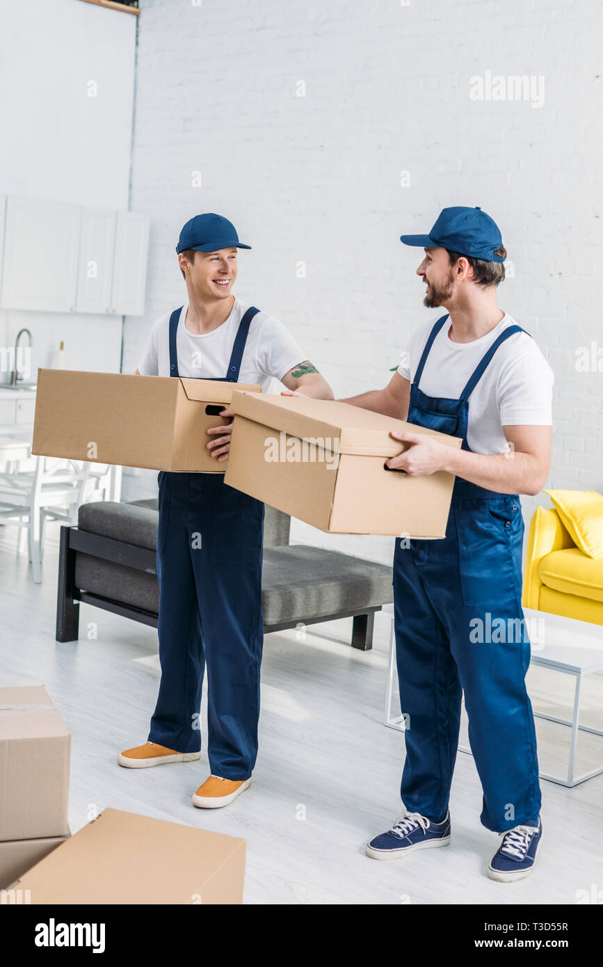 two smiling movers transporting cardboard boxes in apartment Stock Photo