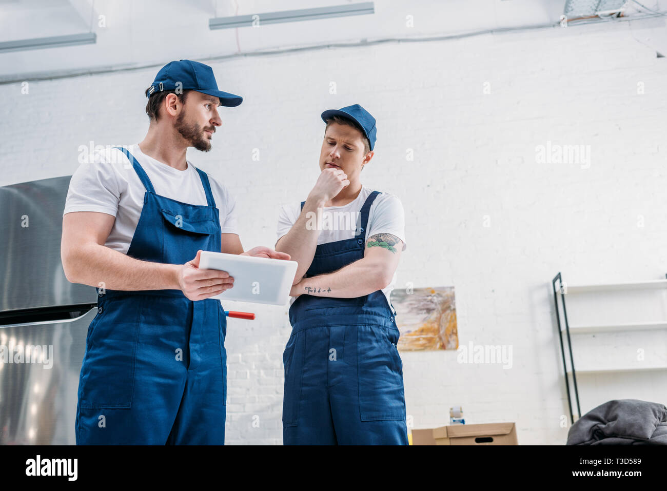 two handsome movers in uniform using digital tablet in apartment with copy space Stock Photo