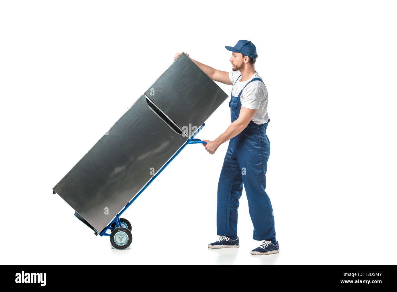 handsome mover in uniform transporting refrigerator on hand truck isolated on white Stock Photo