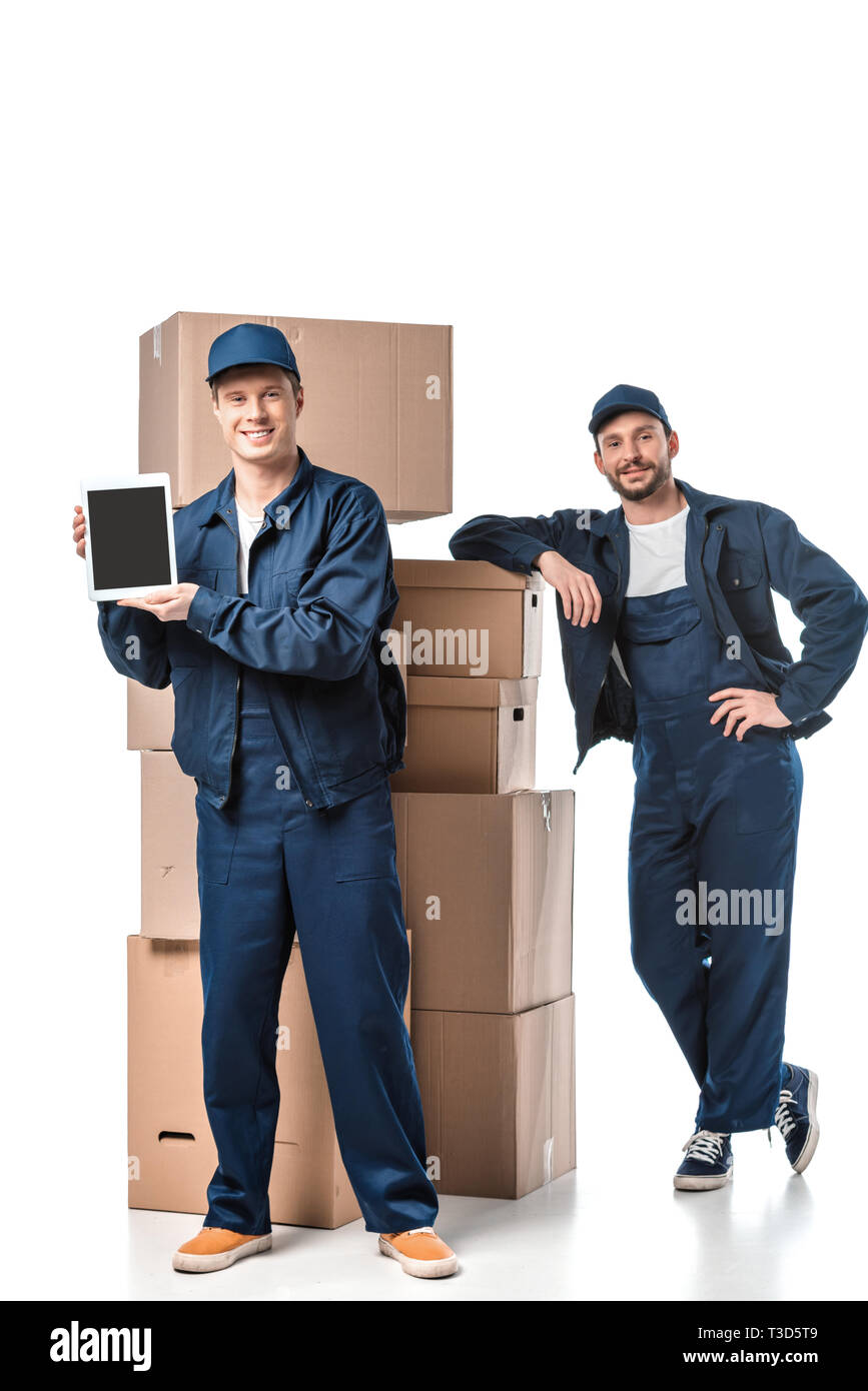 two movers with cardboard boxes looking at camera and presenting digital tablet with blank screen on white Stock Photo
