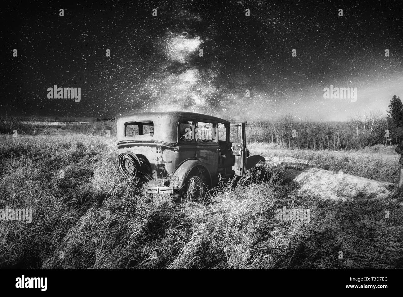 A vintage four door car with one door open abandoned in tall grass