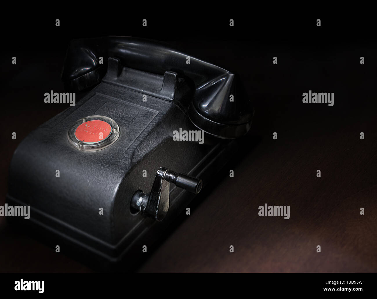 A antique hand crank desk telephone on a dark wooden surface. Low key, copy-space. Stock Photo