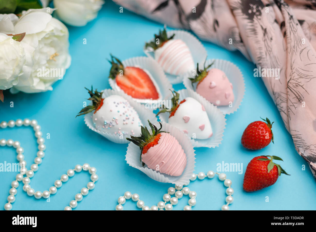 Fresh strawberries covered in white and pink chocolate lie on a turquoise background Stock Photo