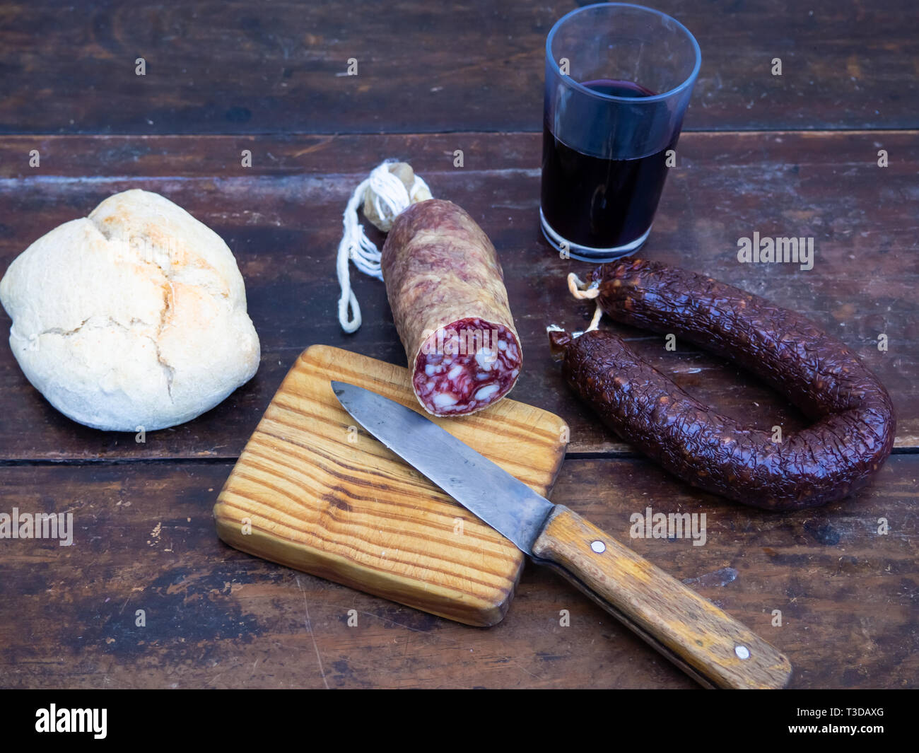 Iberian pork sausages on an old wooden board with a wedge of sheep cheese, an antique knife and a glass of red spanish wine Stock Photo