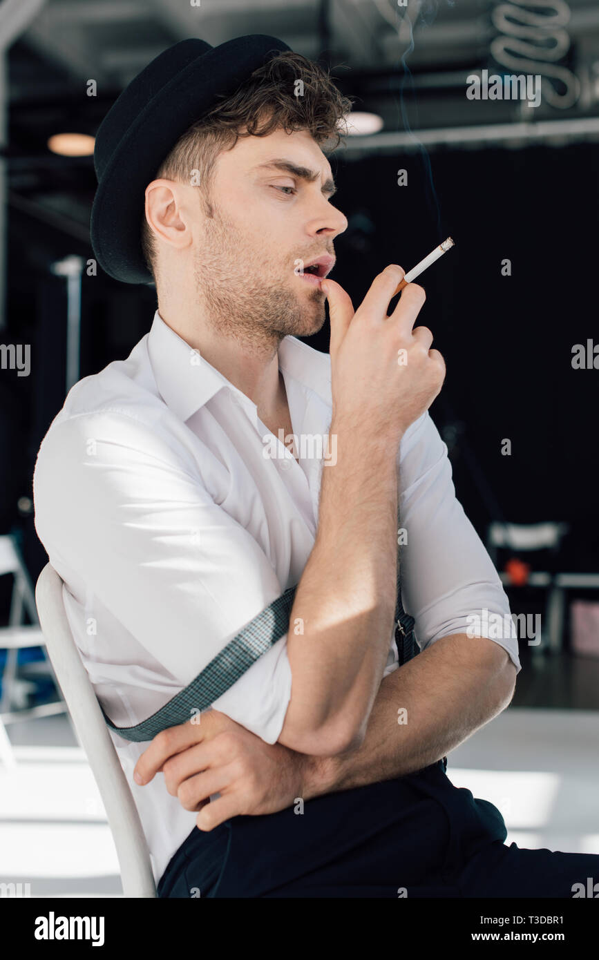 dreamy handsome man in white shirt and black hat smoking cigarette Stock Photo Alamy