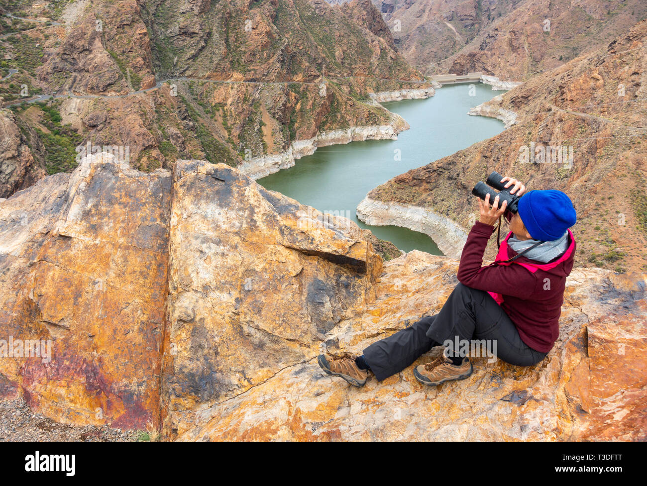 Female hiker/birdwatcher with binoculars above mountain reservoir  (Presa de Parrarillo) in Barranco de Aldea on Gran Canaria, Canary Islands, Spain. Stock Photo