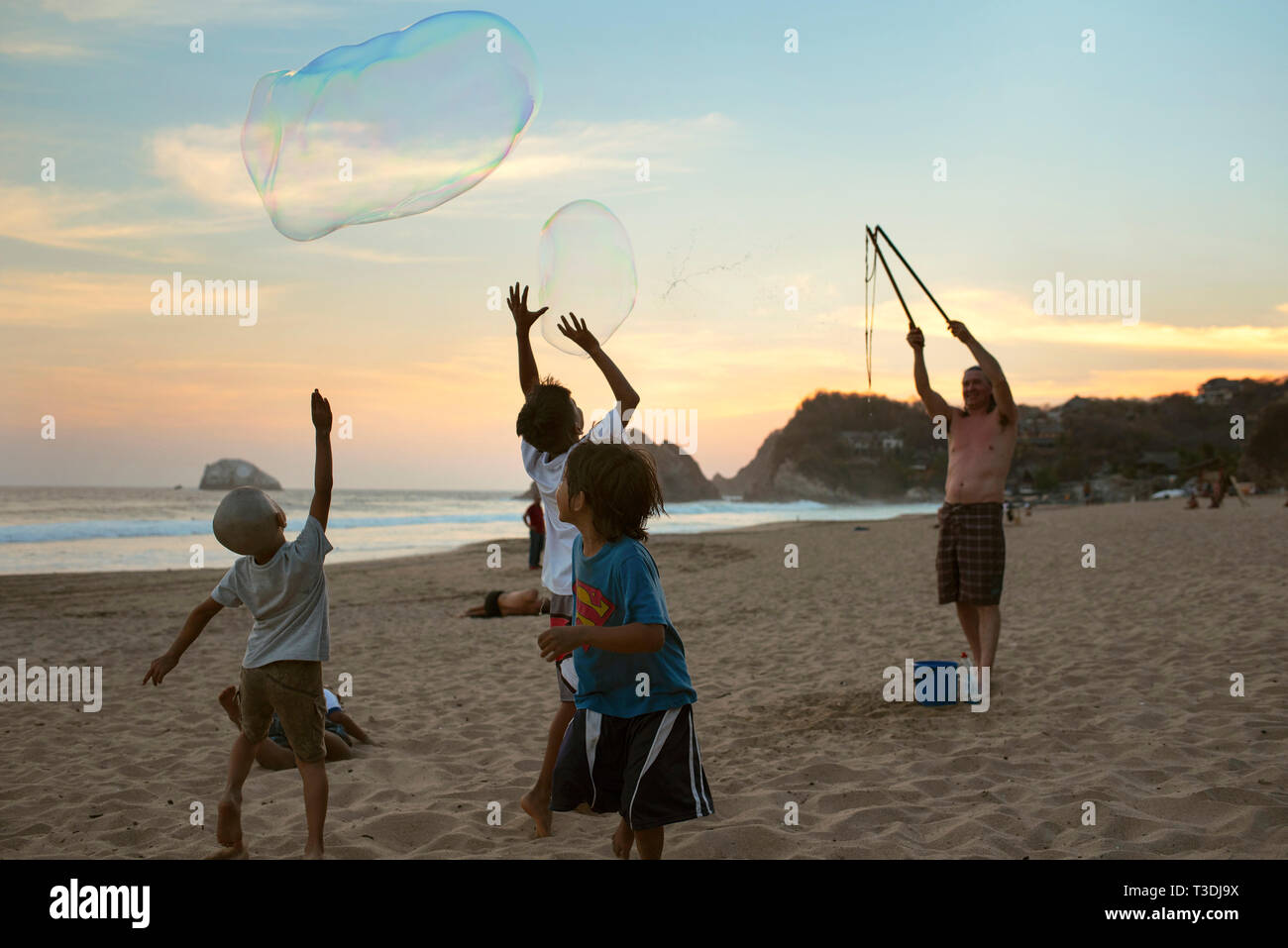 Rear view of local children chasing bubbles on the beach of Zipolite. Oaxaca State, Mexico. Apr 2019 Stock Photo