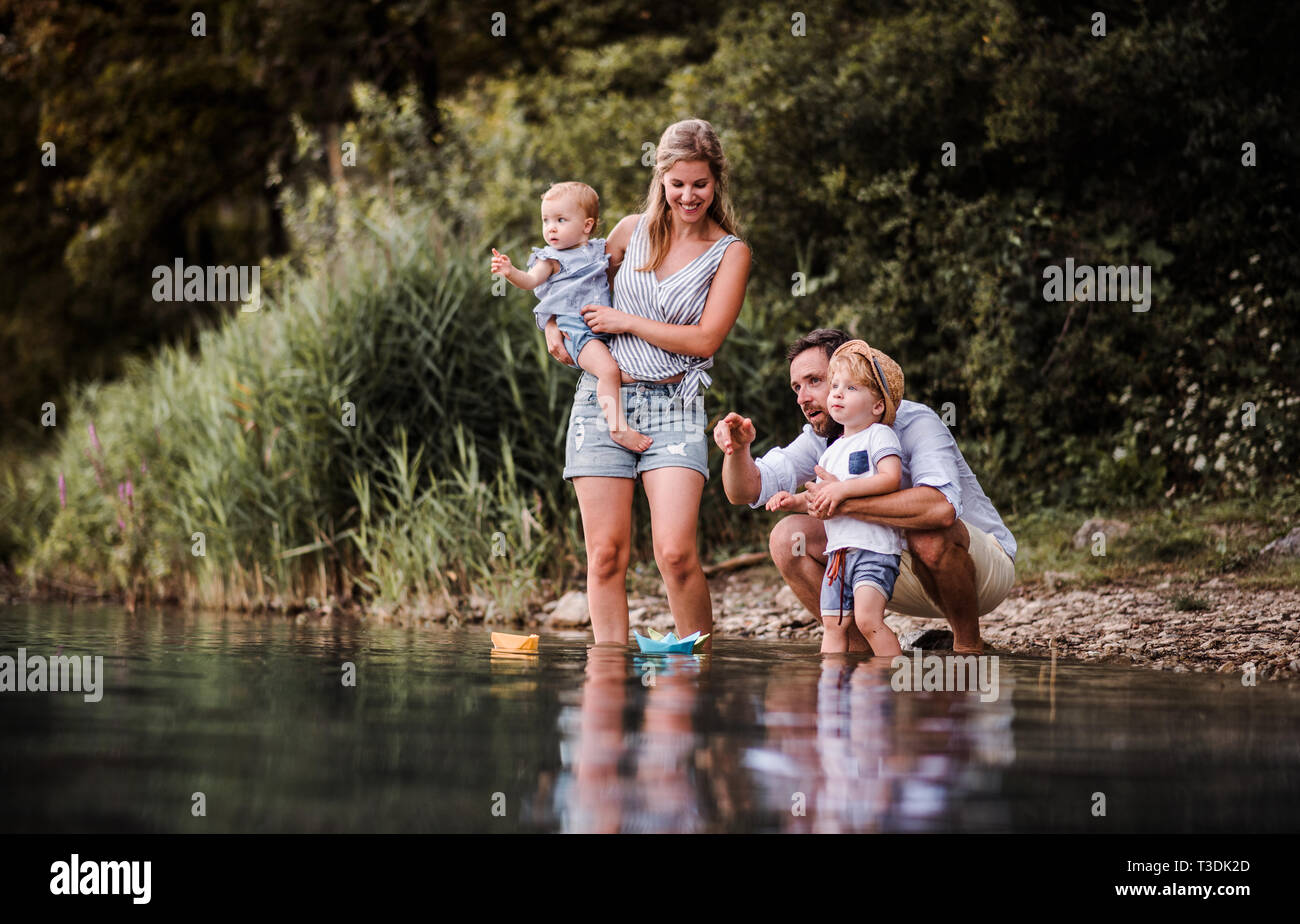 Young family with two toddler children outdoors by the river in summer, playing. Stock Photo