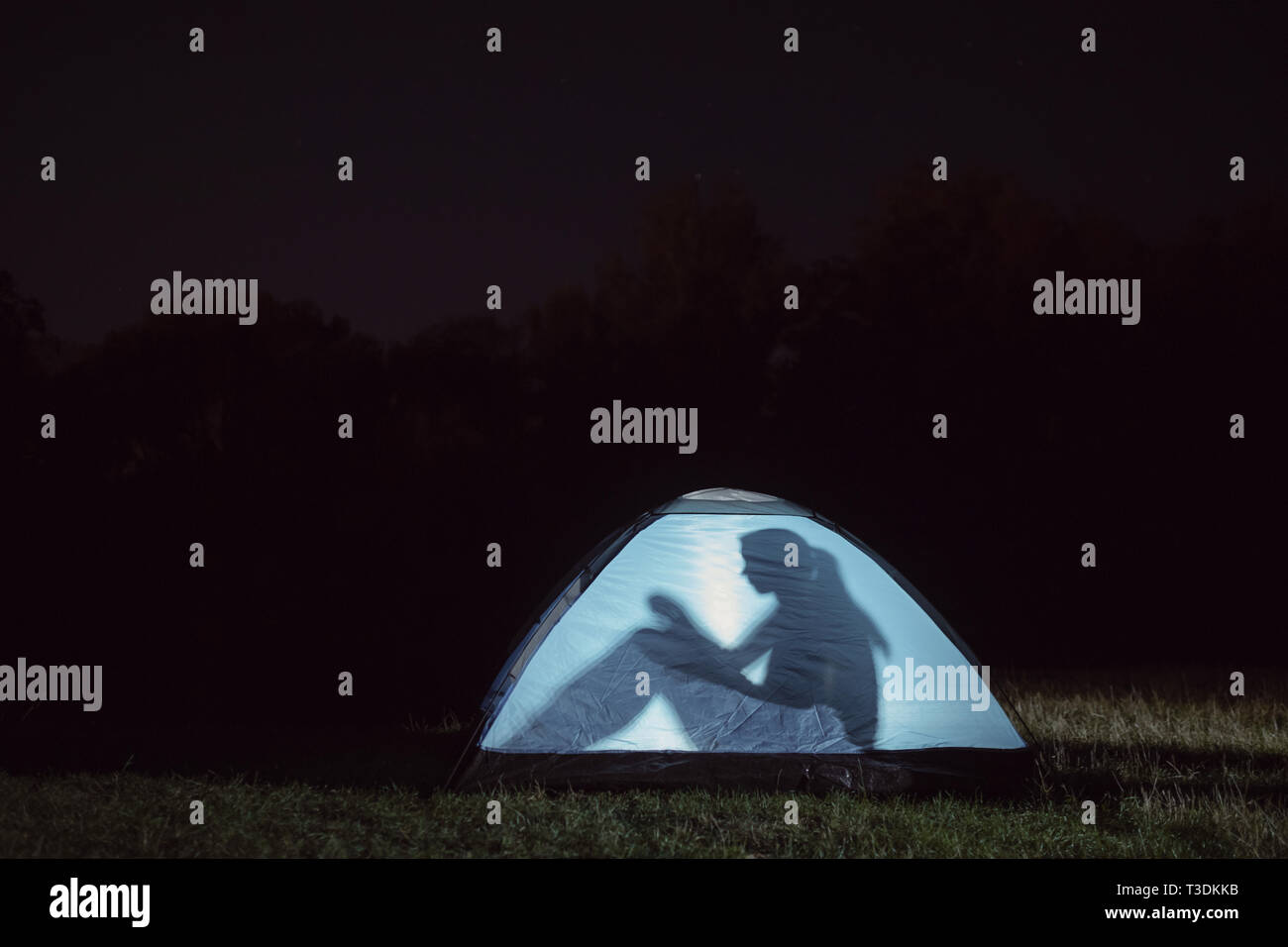 A silhouette of a girl sitting in a tent outdoors at night. Stock Photo