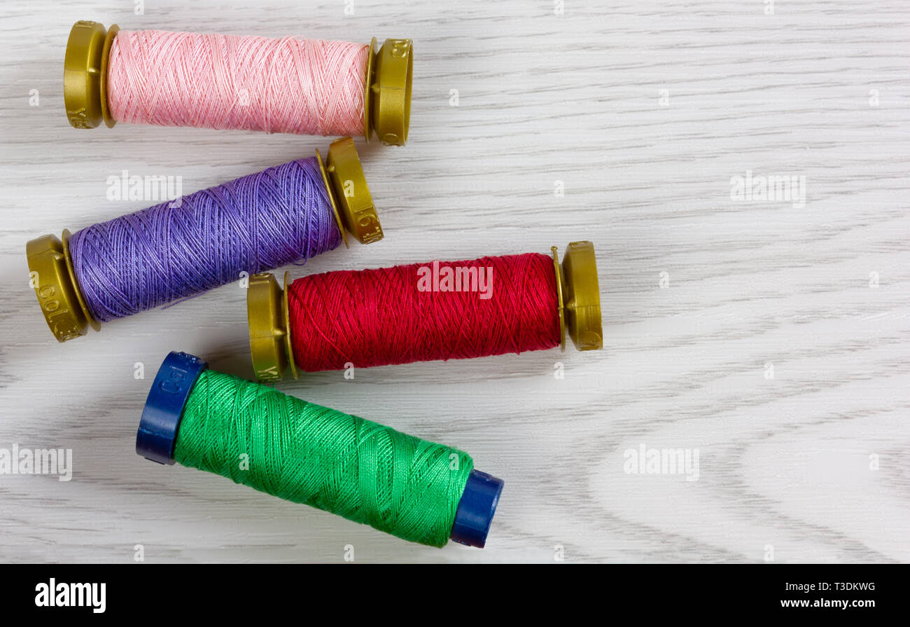 Four thread spools of different colours on a white wooden background ...