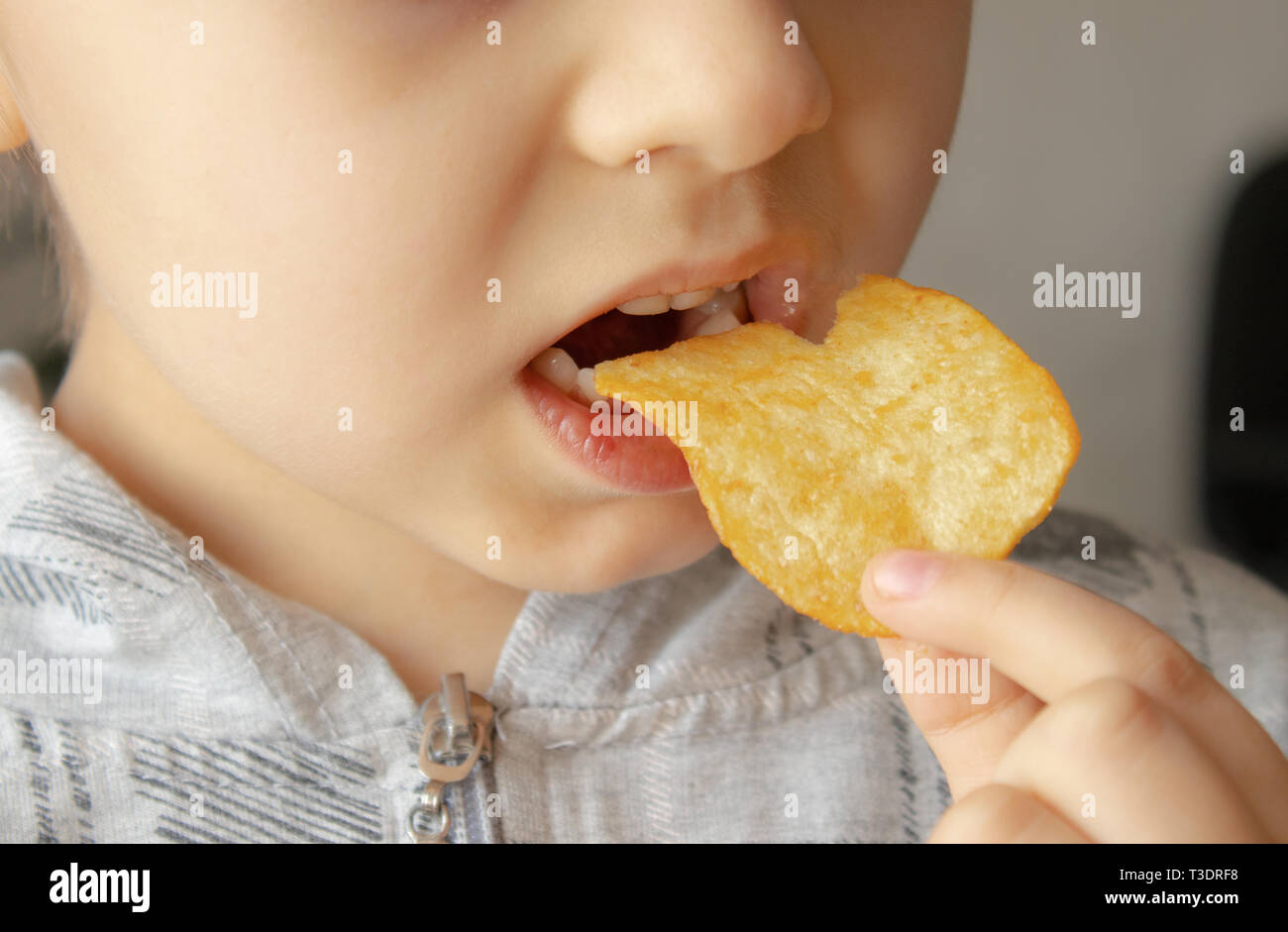 Baby eating chips. Closeup. The child holds the chips. Junk food Stock