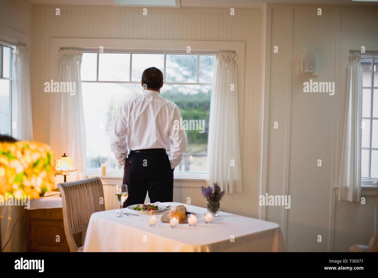 Mature man looking out the window at dinner time Stock Photo - Alamy