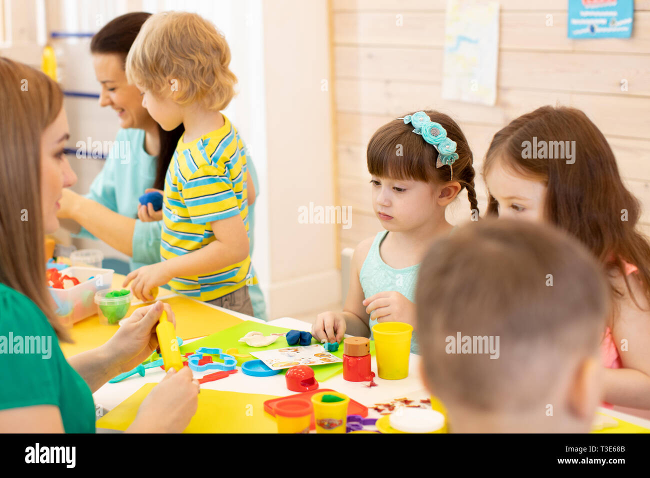Teacher teaches group of children modeling clay in playroom at daycare or kindergarten Stock