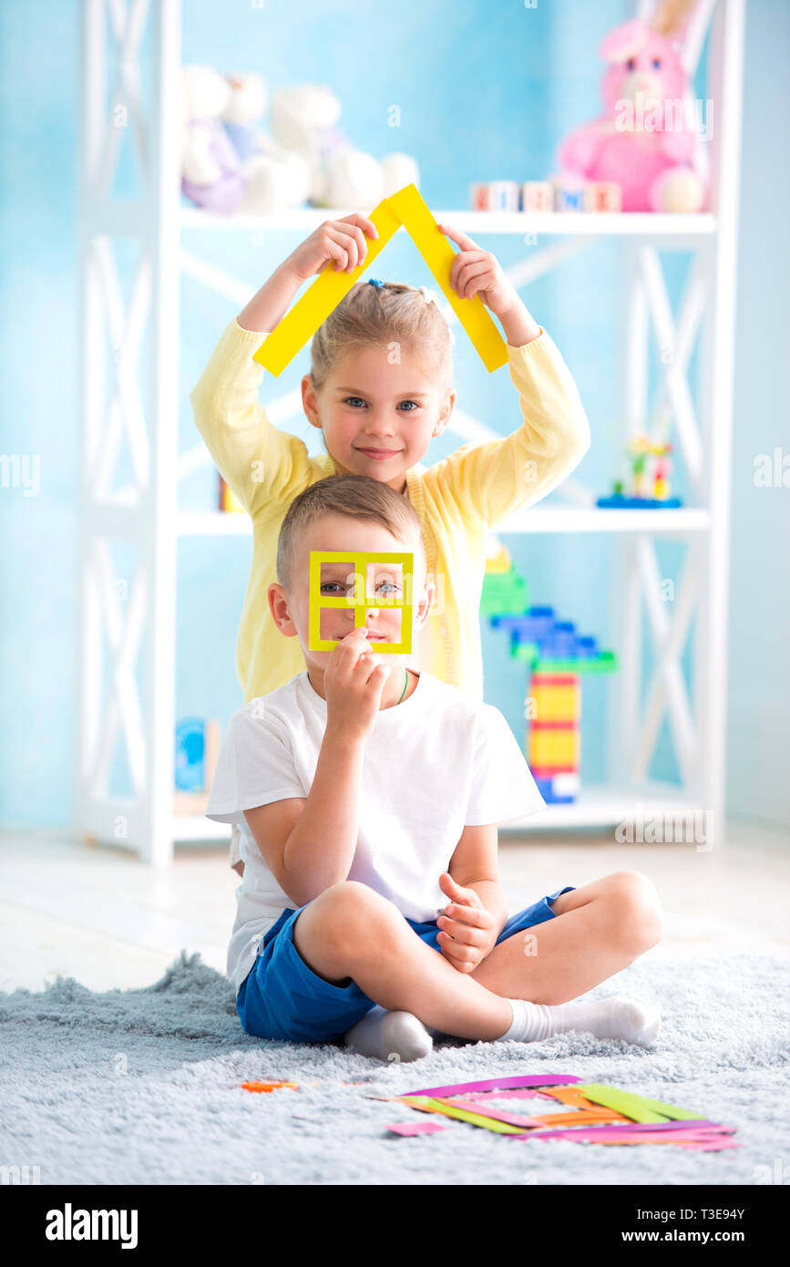 A little girl with a boy is sitting on the floor and holding a house of ...