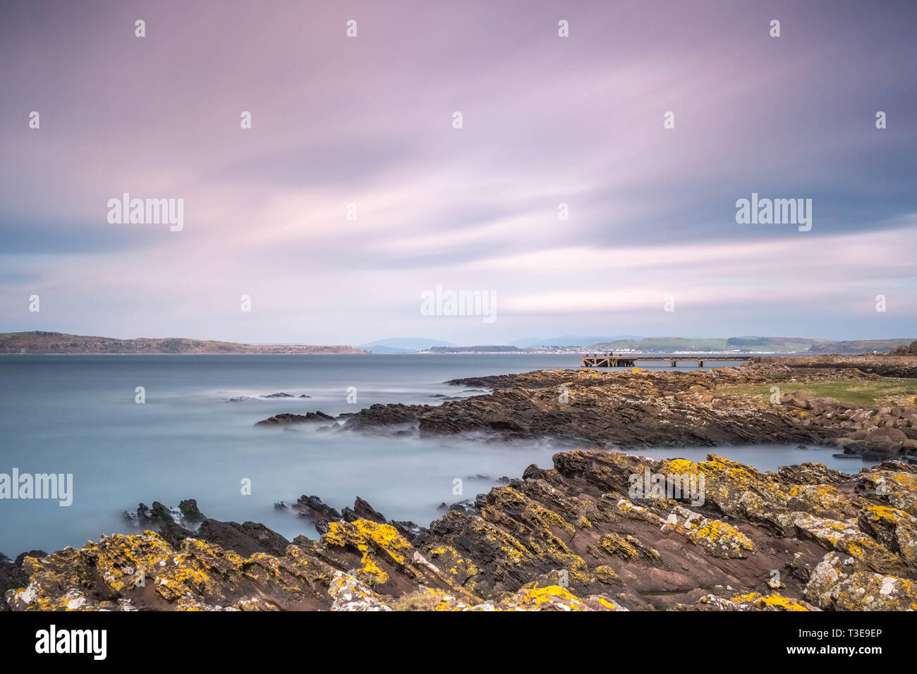 Looking over the rocky harbour  to the old jetty at Portencross in Seamill West Kilbride on a cold bright day in Scotland. Image is a long exposure to Stock Photo