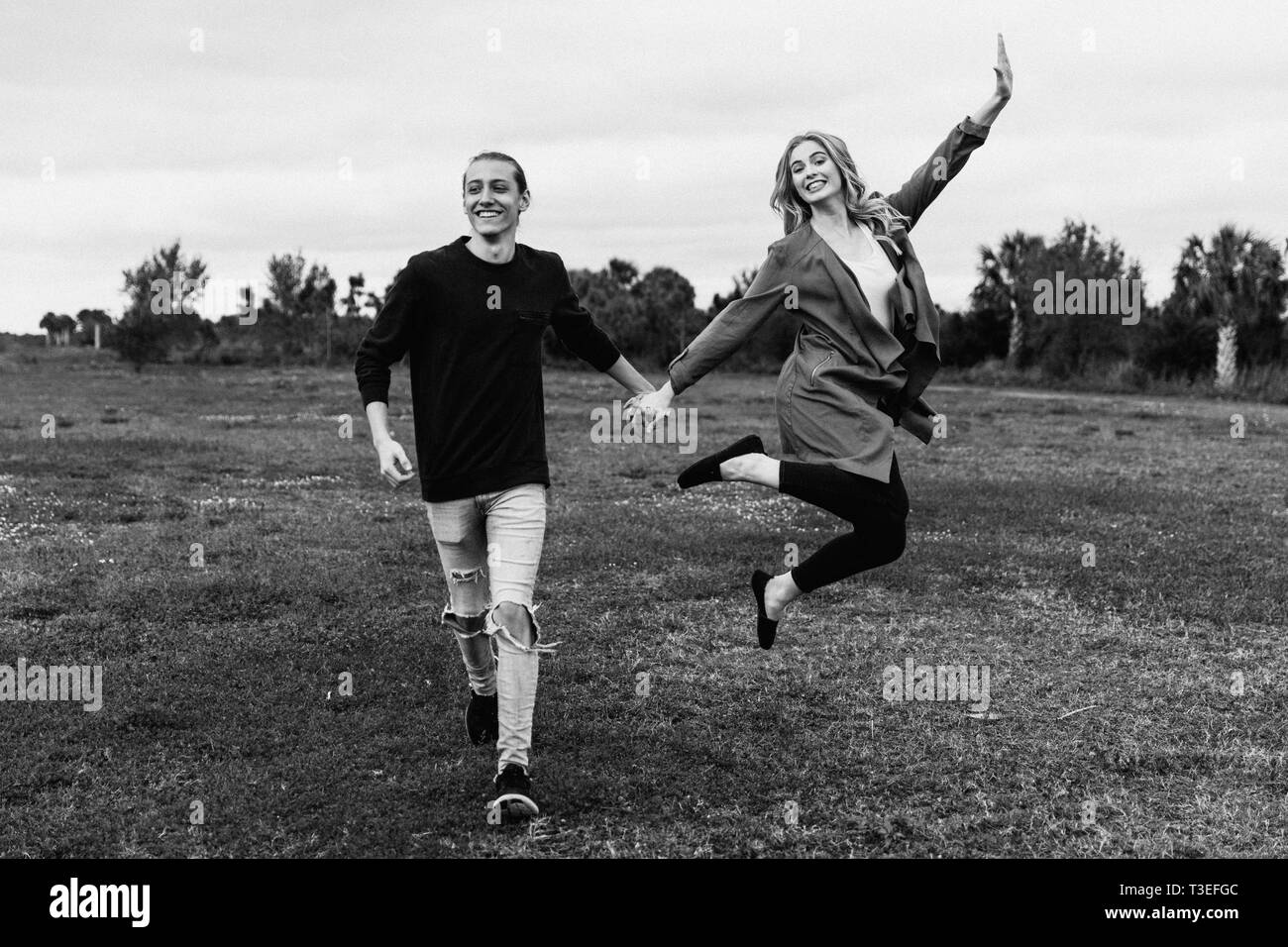 Young Couple in Love Running in a Big Open Outdoor Field in the Spring Holding Hands and Laughing Stock Photo