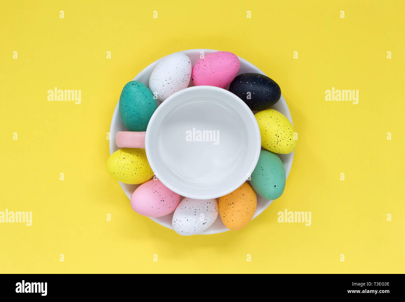 Colourful Easter eggs around a tea cup, on a yellow background Stock Photo