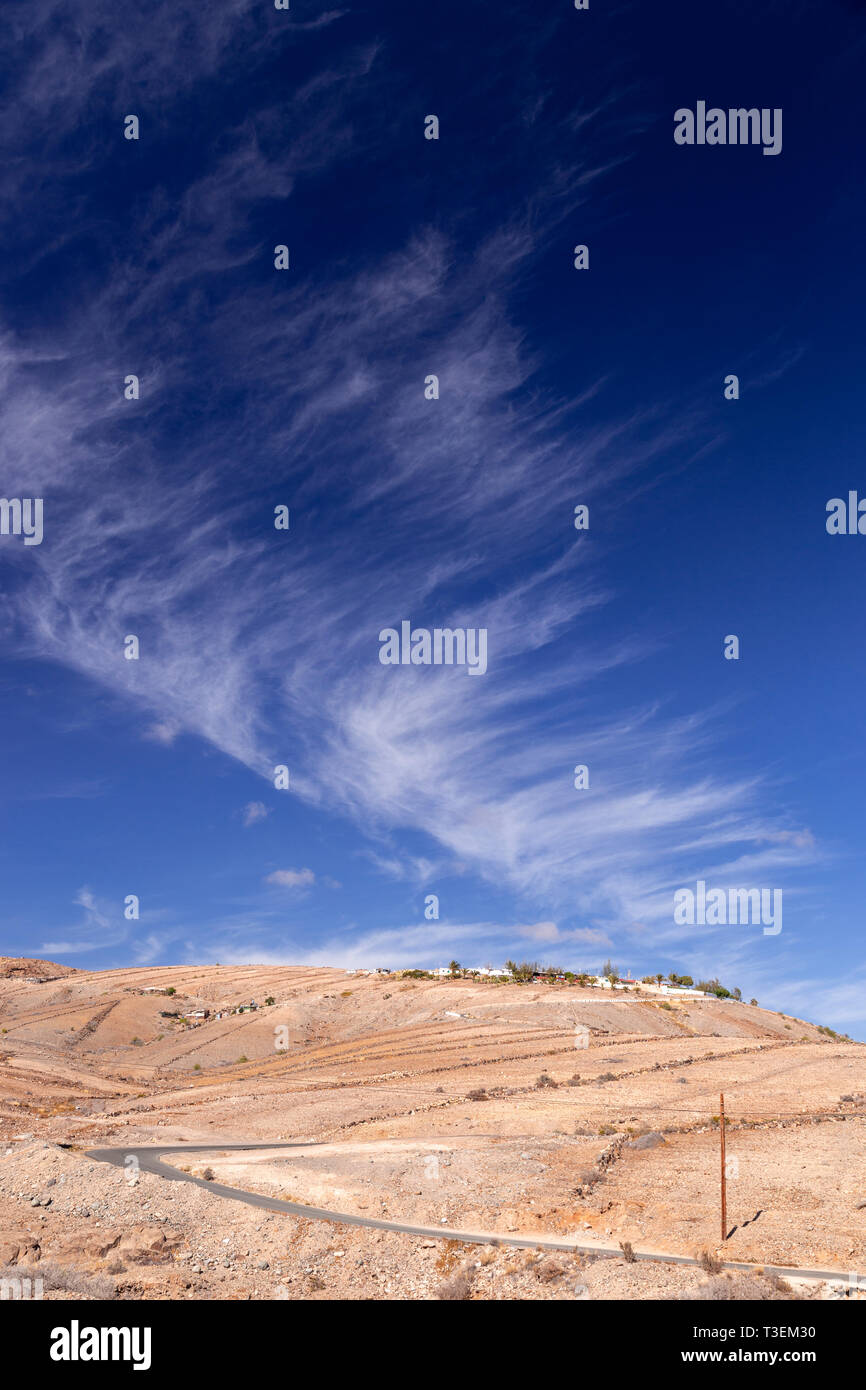 Road through dry landscape at Meloneras, Gran Canaria, Canary Islands with cirrus clouds overhead Stock Photo