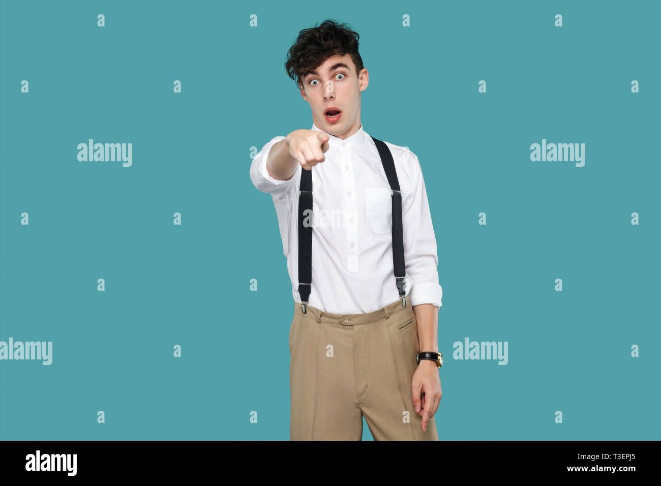 Shocked man pointing and looking at camera. Portrait of handsome hipster curly young businessman in classic casual white shirt and suspender standing. Stock Photo