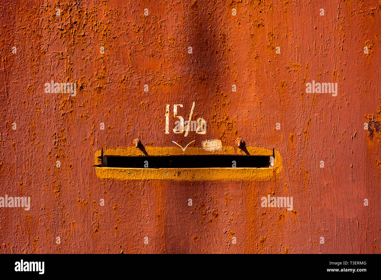 Close-up old red painted metal door with number fifteen fractions two and mail hole. Horizontal texture of cracked paint on rusty steel Stock Photo