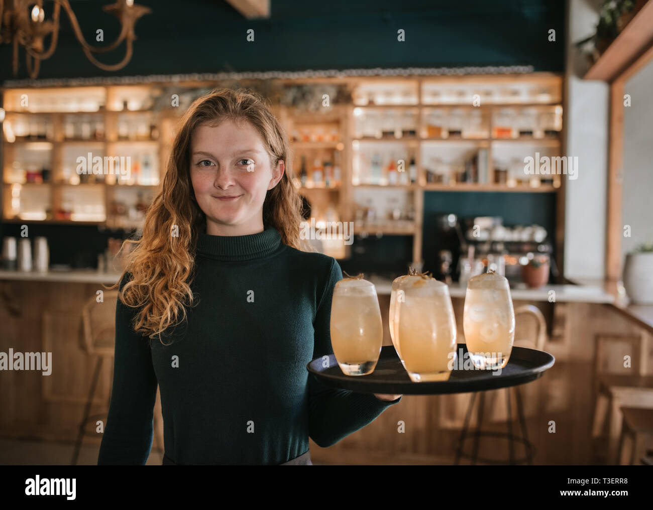 Smiling bar waitress holding a tray of drinks Stock Photo