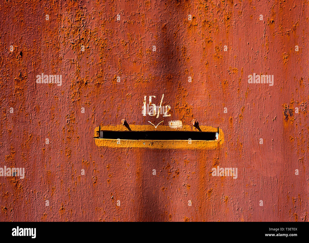 Old red painted metal door with number fifteen fractions two and mail hole with orange edge Stock Photo