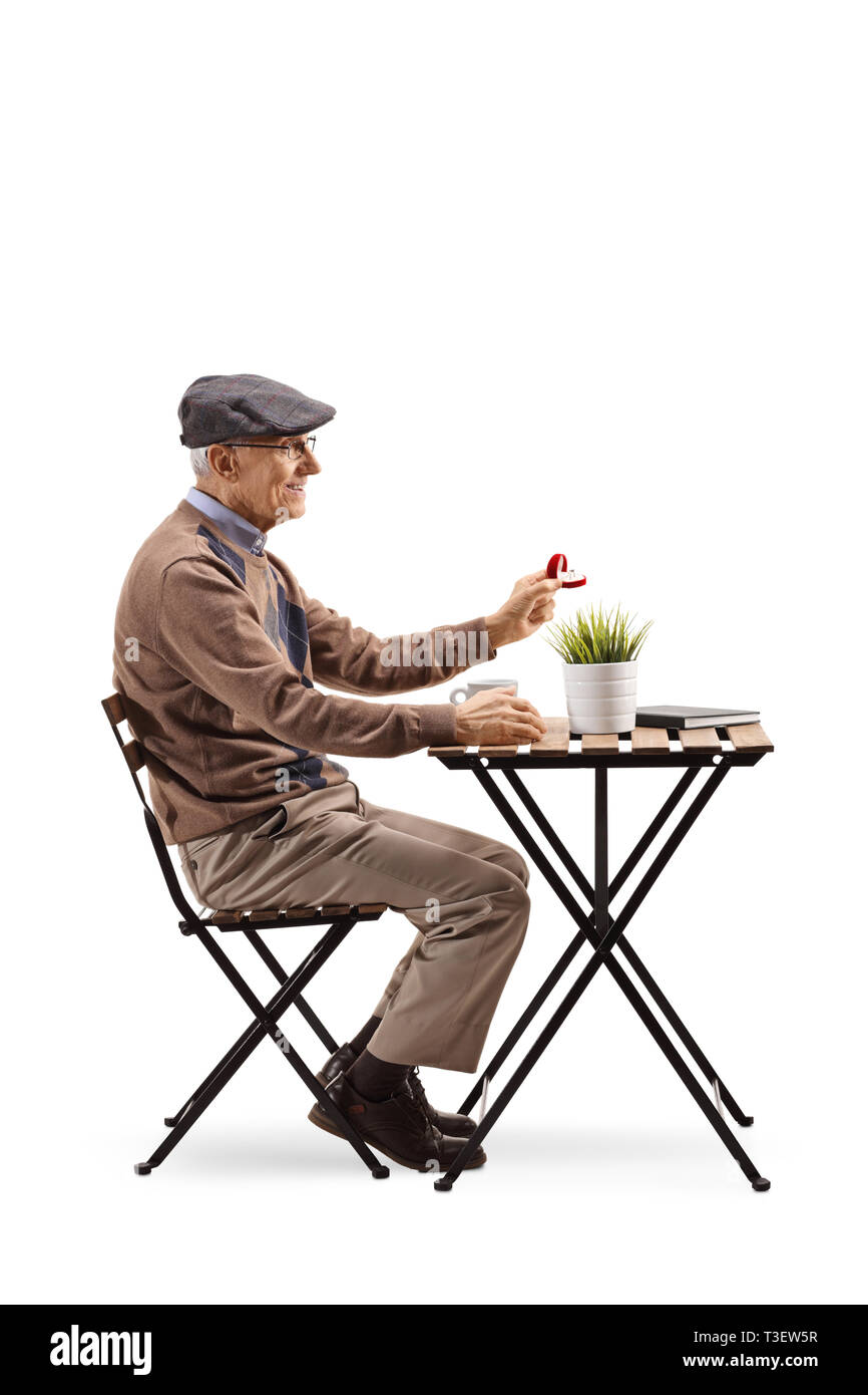 Full length profile shot of a senior man sitting at a cafe and holding a ring in a box isolated on white background Stock Photo