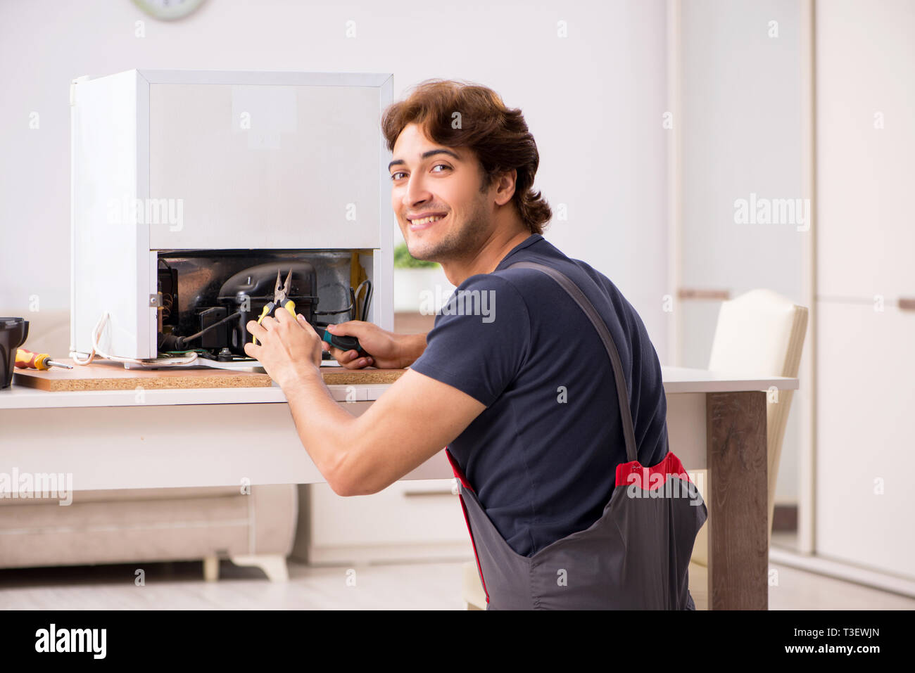 Young handsome contractor repairing fridge Stock Photo